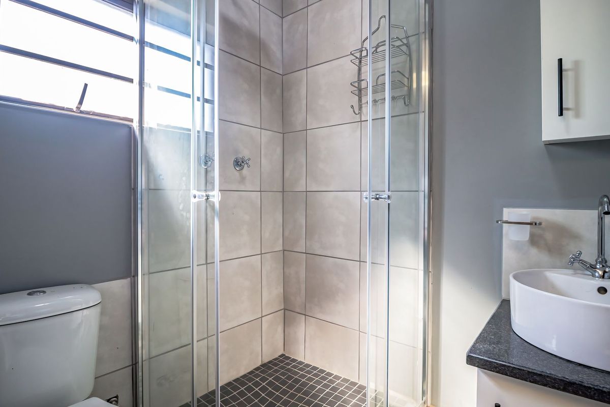 A modern bathroom featuring a glass-enclosed shower with tiled walls, a white vanity basin with a mixer tap, and a standard toilet.