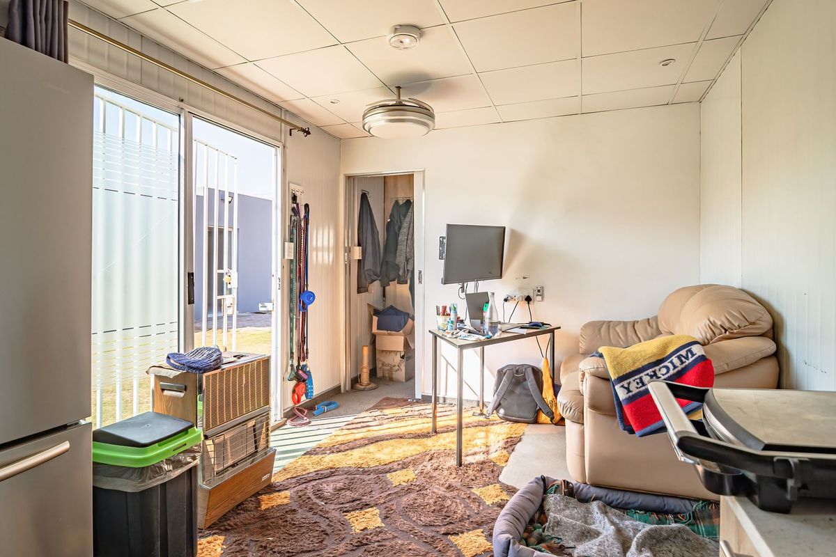 A compact living area featuring a sliding glass door with security gate, built-in closet space, and suspended ceiling tiles.
