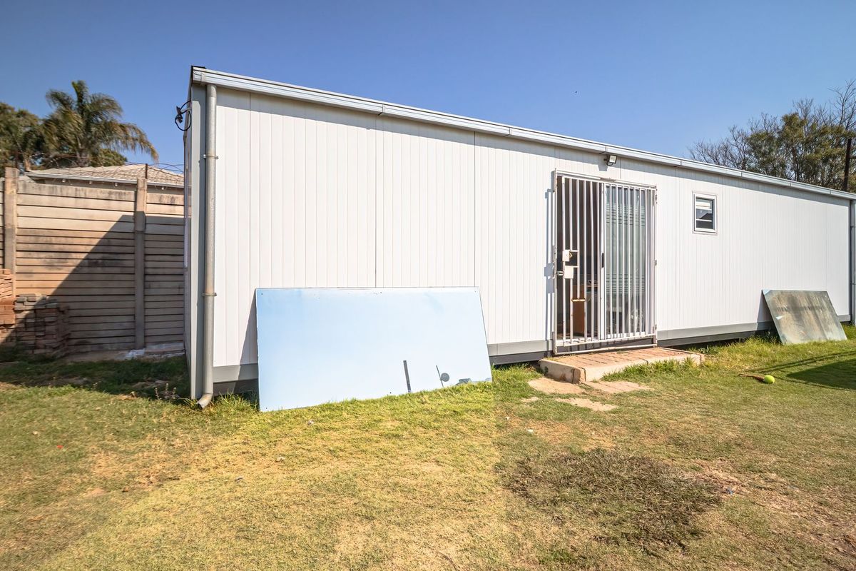 A view of the rear exterior of a modular-style building featuring metal cladding, a security gate entrance, and a concrete step.