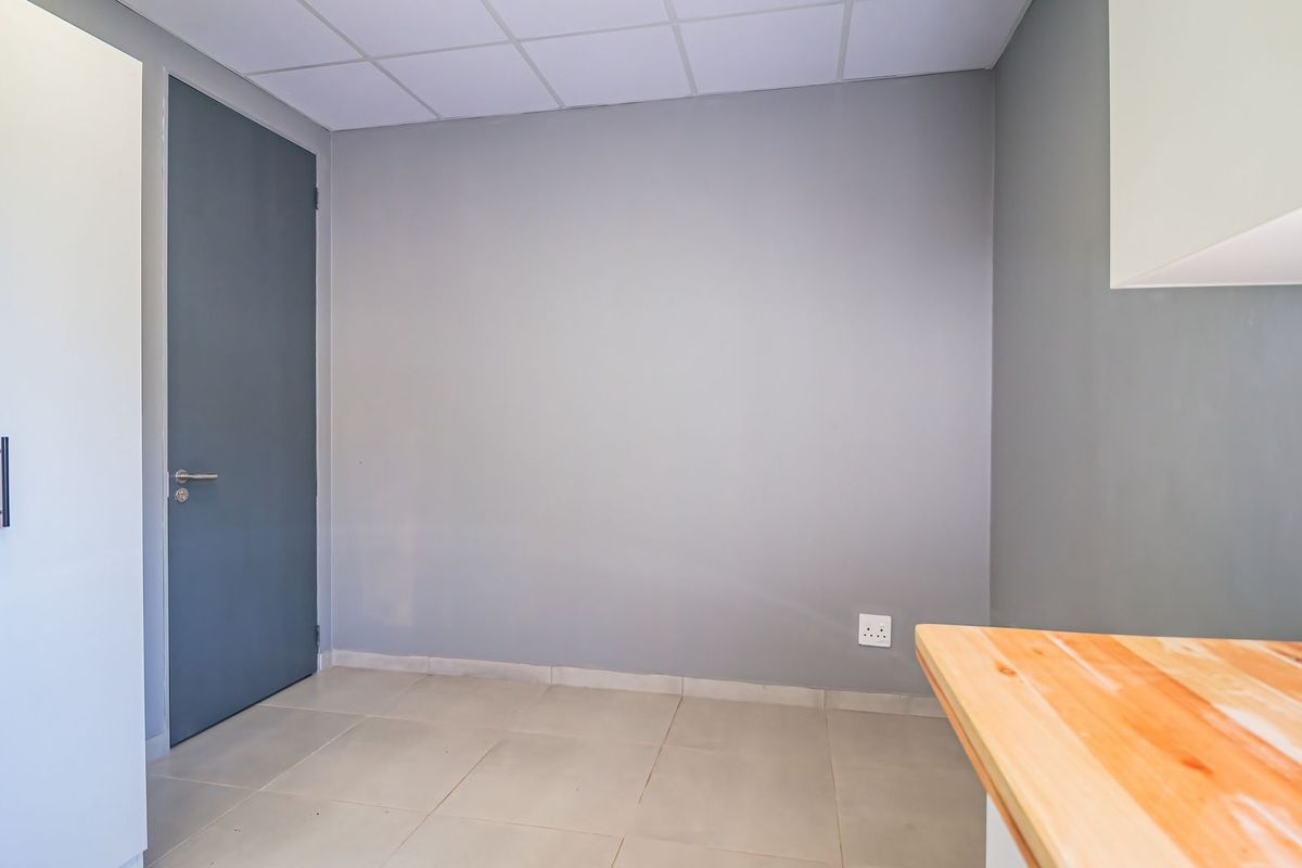 A clean, empty bedroom featuring neutral grey walls, tiled flooring, a drop ceiling, and a built-in wardrobe with a timber countertop workspace.