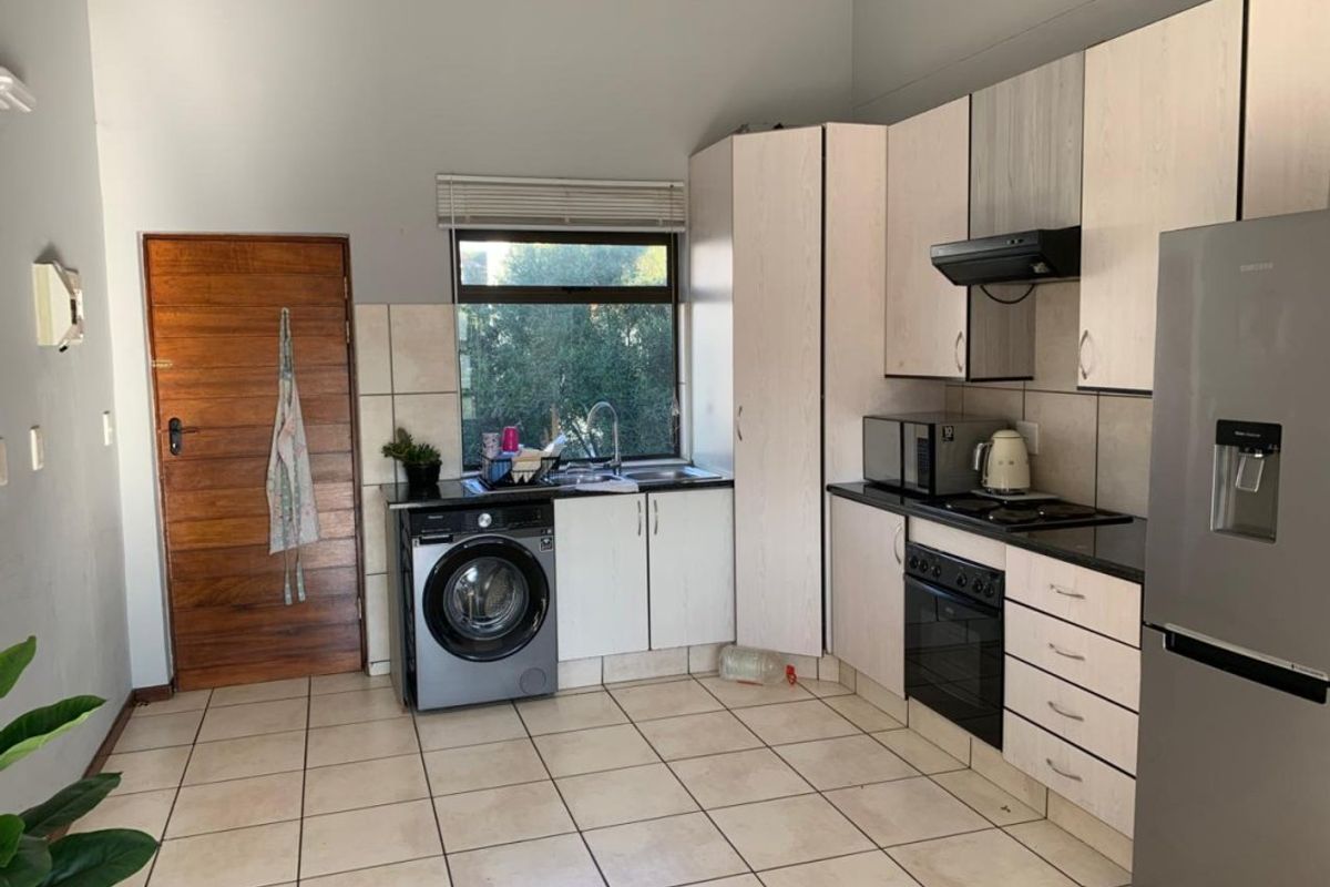 Functional kitchen featuring built-in cabinetry, integrated oven and hob, tiled flooring, and direct access to the exterior via a timber door.