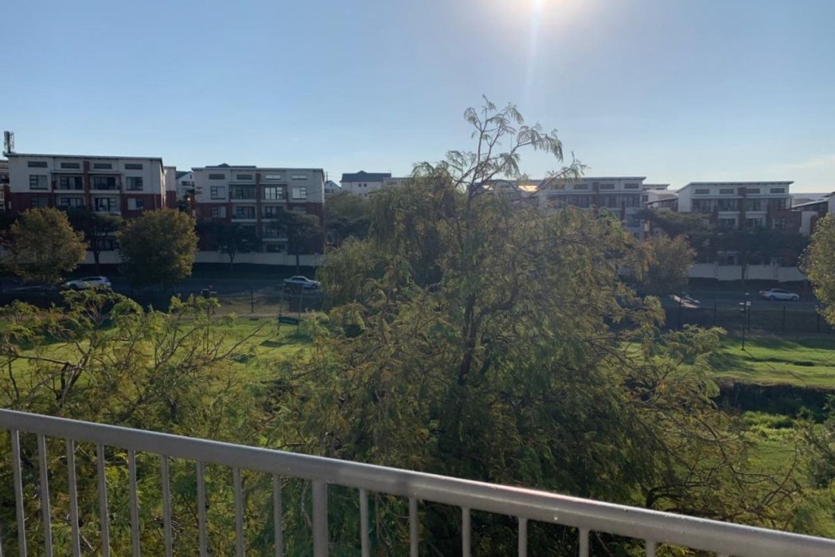 An elevated view overlooking a green park area and surrounding residential complex, featuring a metal safety balustrade in the foreground.