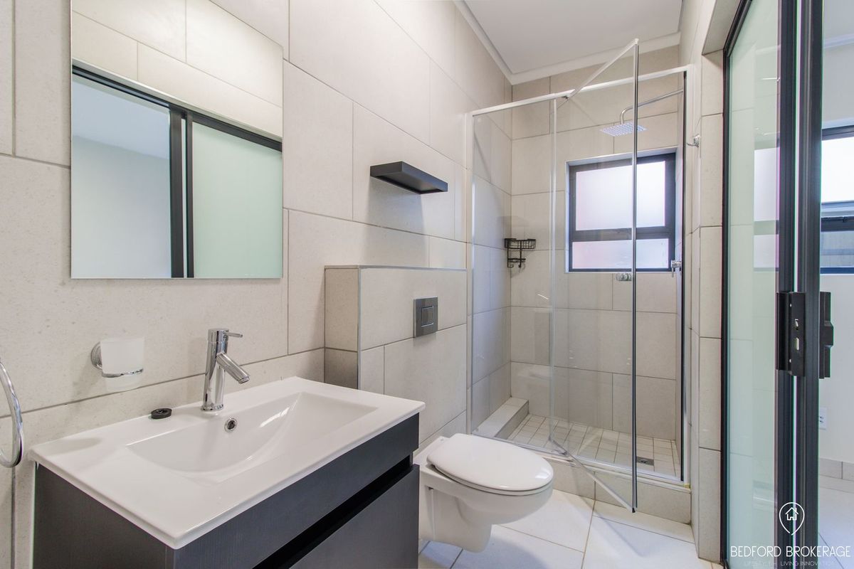 Modern bathroom featuring a wall-hung toilet, vanity with basin, and a glass-enclosed shower with neutral floor-to-ceiling tiling.