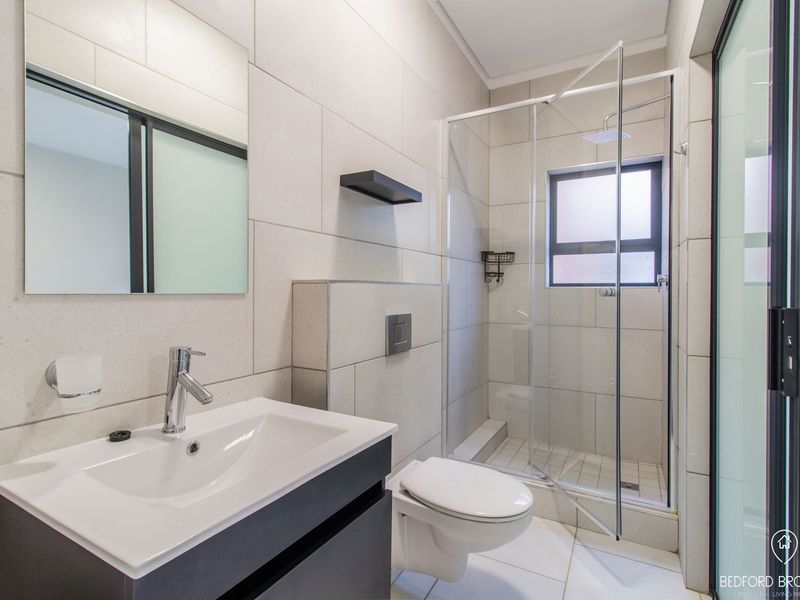 Modern bathroom featuring a wall-hung toilet, vanity with basin, and a glass-enclosed shower with neutral floor-to-ceiling tiling.