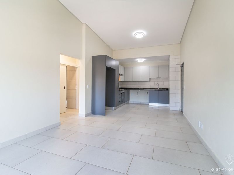An open-plan kitchen and living area featuring modern grey cabinetry, tiled flooring, and integrated appliances in a clean, neutral space.
