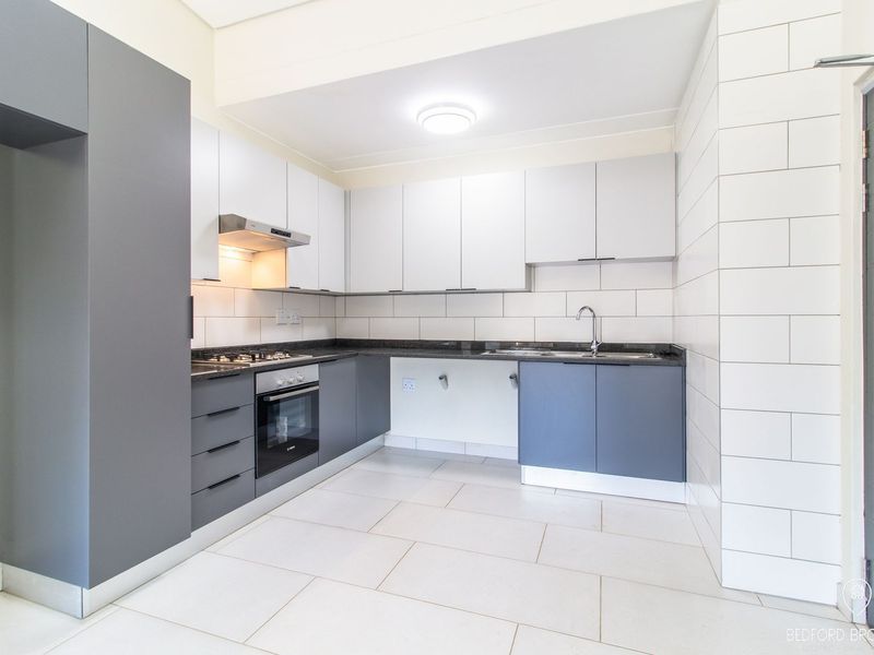 Modern kitchen featuring sleek grey and white cabinetry, granite countertops, built-in oven, gas hob, and a tiled splashback in a clean, contemporary finish.