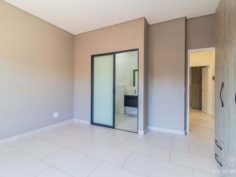 Spacious bedroom featuring neutral tones, modern tiled flooring, built-in cupboards, and a sleek sliding door leading to an en-suite bathroom.