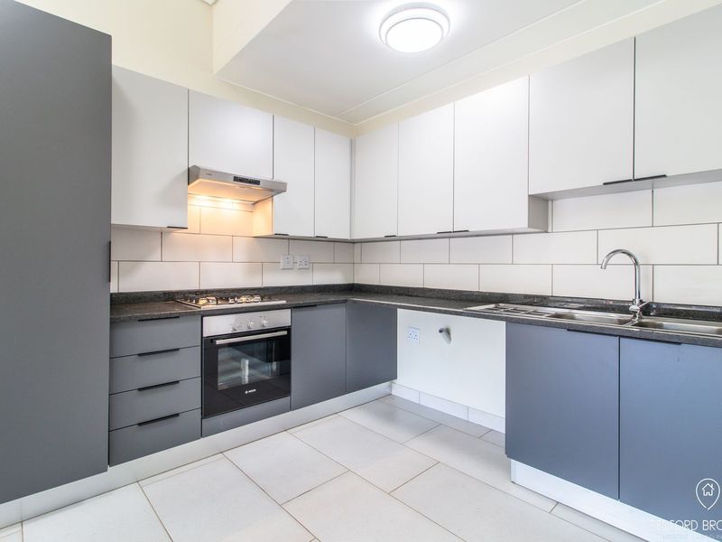 Modern kitchen featuring two-tone cabinetry, stone countertops, built-in oven, gas hob, extractor fan, and a stainless steel sink with tiled backsplash.