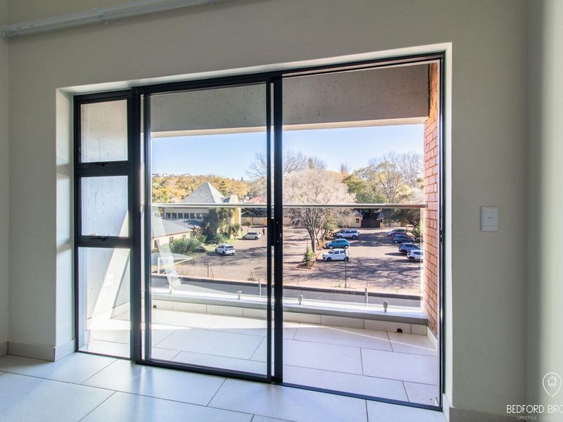 A bright, modern balcony featuring tiled flooring, a sleek glass balustrade, and sliding door access, offering an elevated view of the surrounding area.