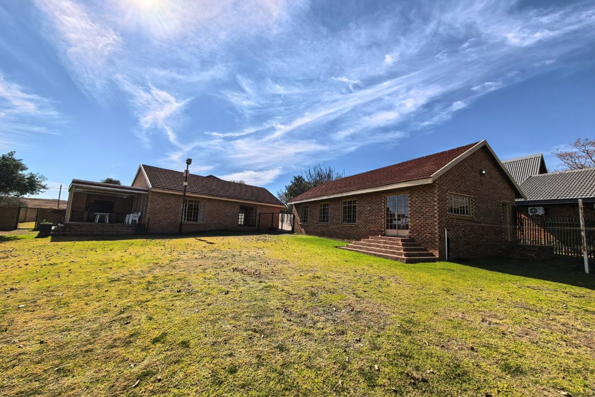 Rear view of the property featuring face brick construction, tiled roofing, and a spacious lawn area with a covered patio.