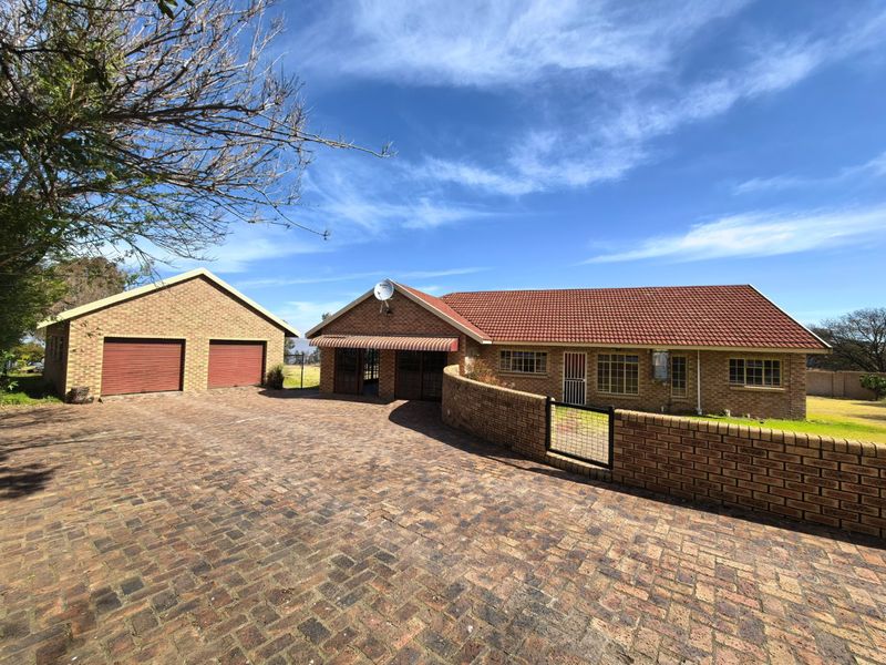 Front view of a face brick house featuring a tiled roof, a spacious paved driveway, and a detached double garage with a brick boundary wall.