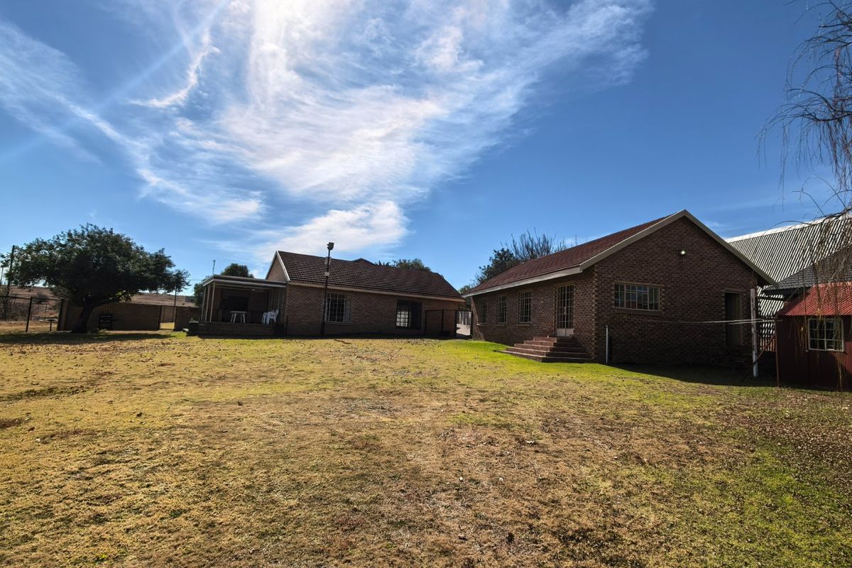 Rear view of the property showing brick construction, tiled roofing, and a spacious backyard area with a covered patio.
