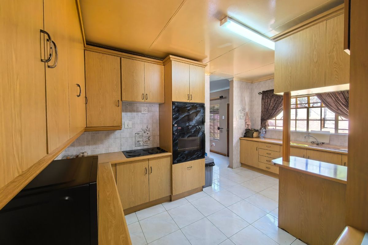 A functional kitchen featuring wood-look cabinetry, built-in oven, electric hob, and tiled flooring, offering a practical layout with ample storage space.