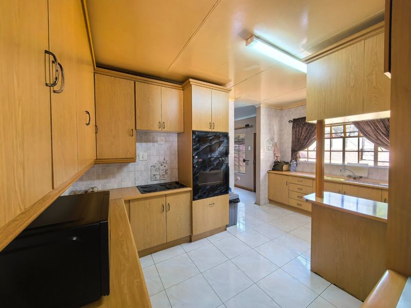 A functional kitchen featuring wood-look cabinetry, built-in oven, electric hob, and tiled flooring, offering a practical layout with ample storage space.