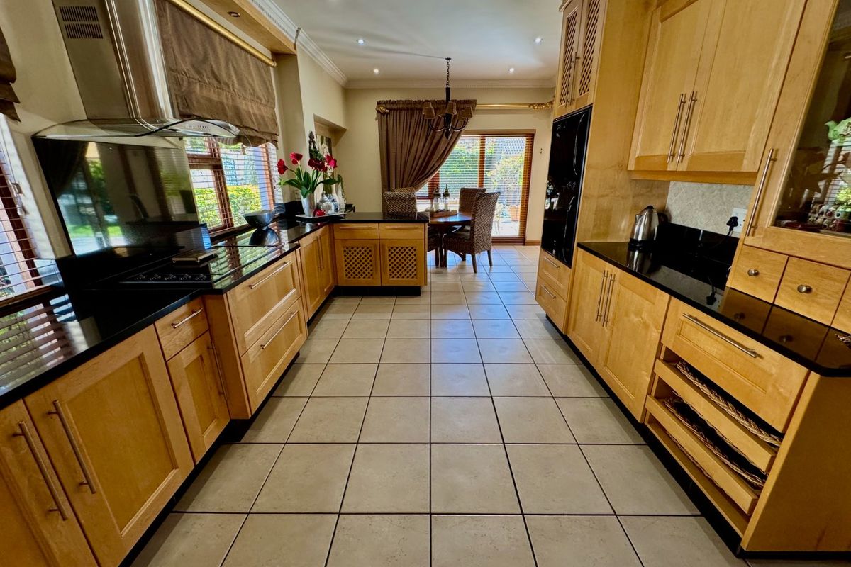 A spacious kitchen featuring light wood cabinetry, black granite countertops, built-in appliances, and ceramic tile flooring, flowing into an adjacent dining area.