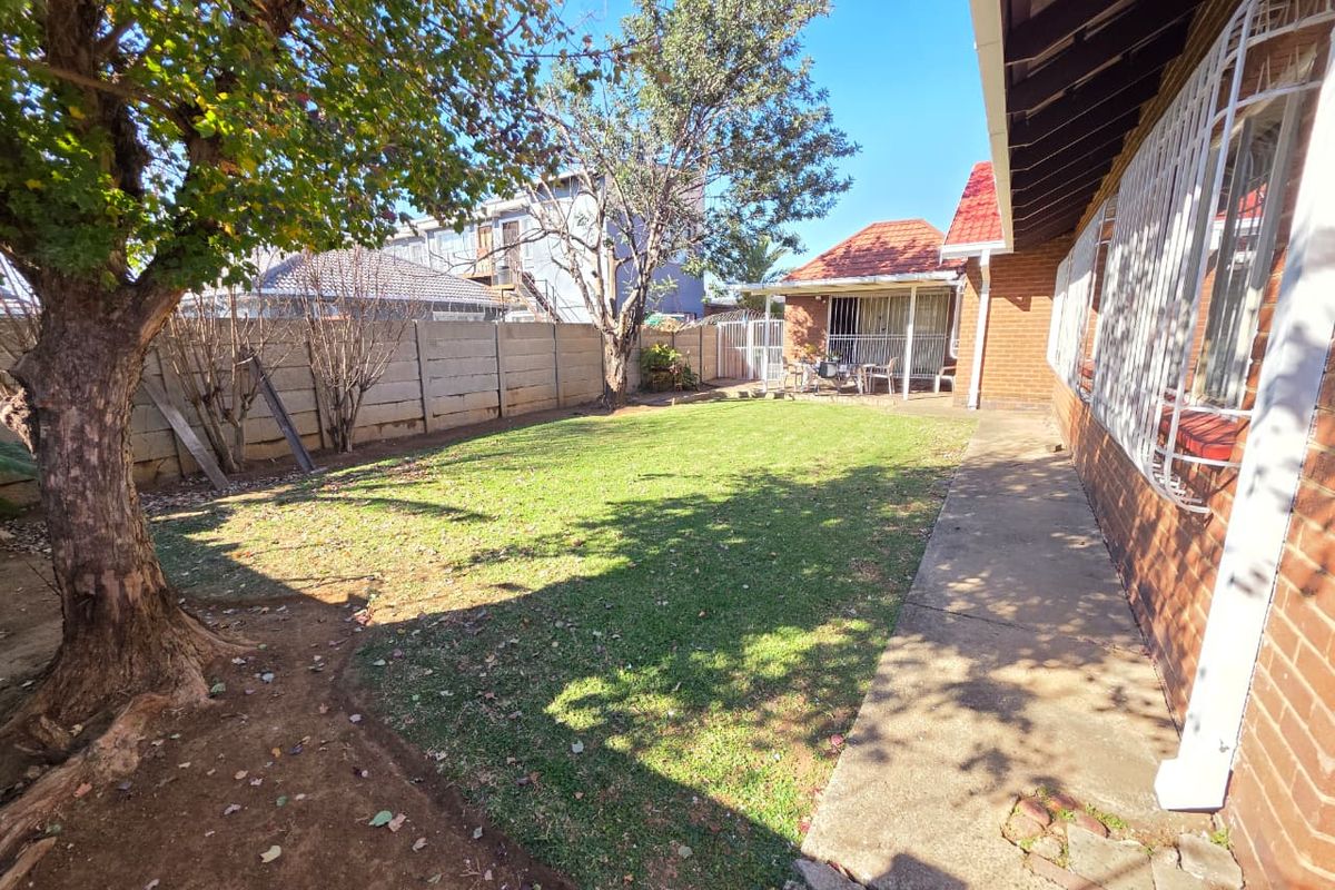 A rear garden area featuring a lawn, concrete pathway, and brick exterior wall with security bars on the windows.