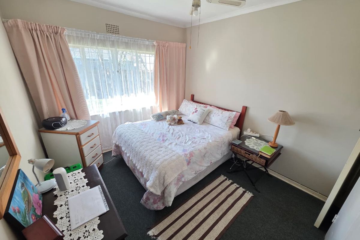 A functional bedroom featuring carpet flooring, a ceiling fan, and large windows with curtains, offering a comfortable and well-lit living space.
