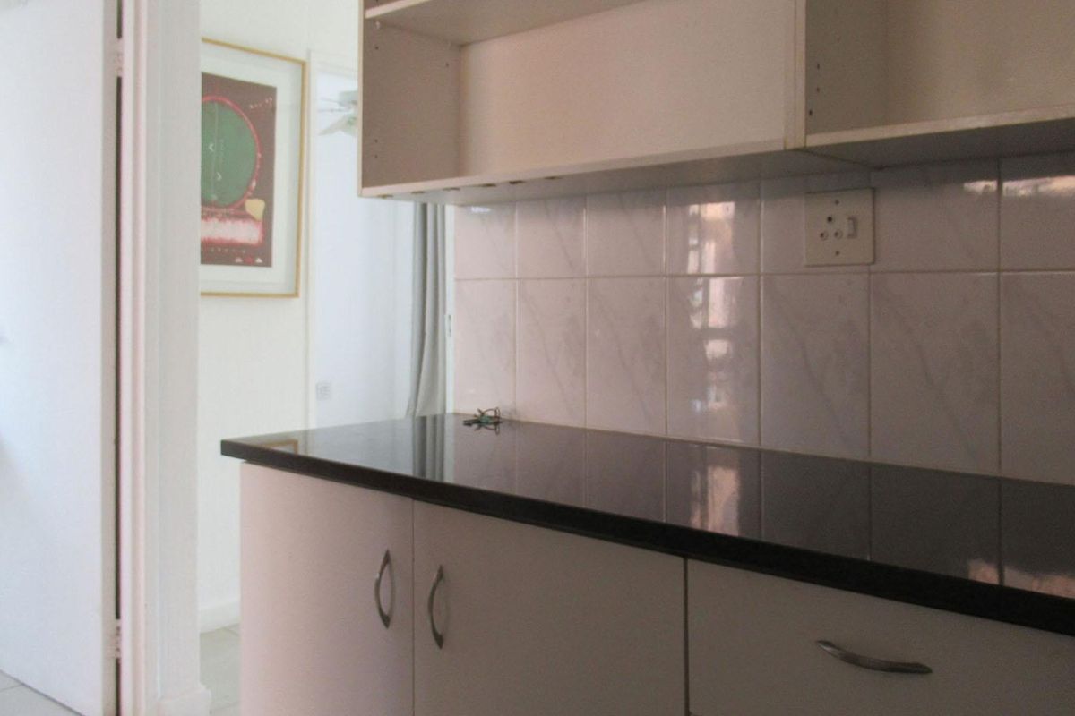 A compact kitchen area featuring dark granite countertops, white cabinetry, and a tiled backsplash, with an adjacent view into a bathroom area.