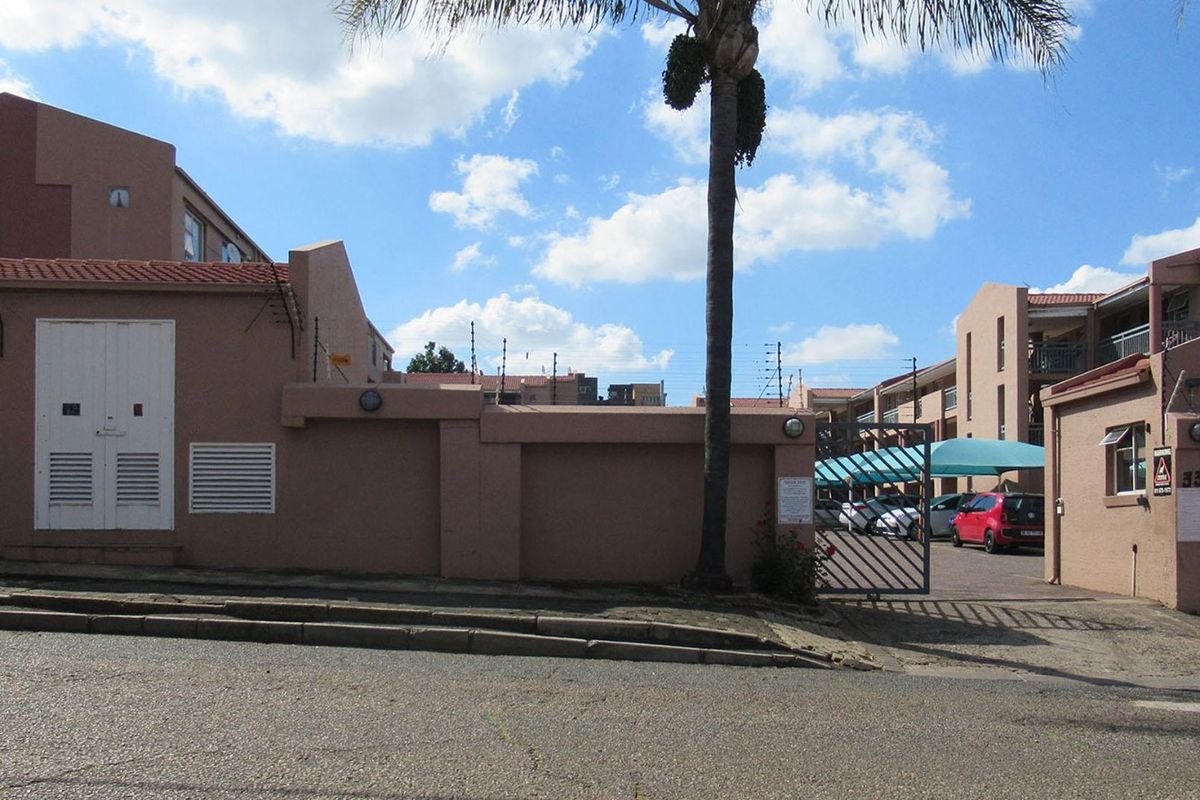 Street view of the apartment complex entrance featuring a secure gated access point, perimeter wall with electric fencing, and covered parking area.