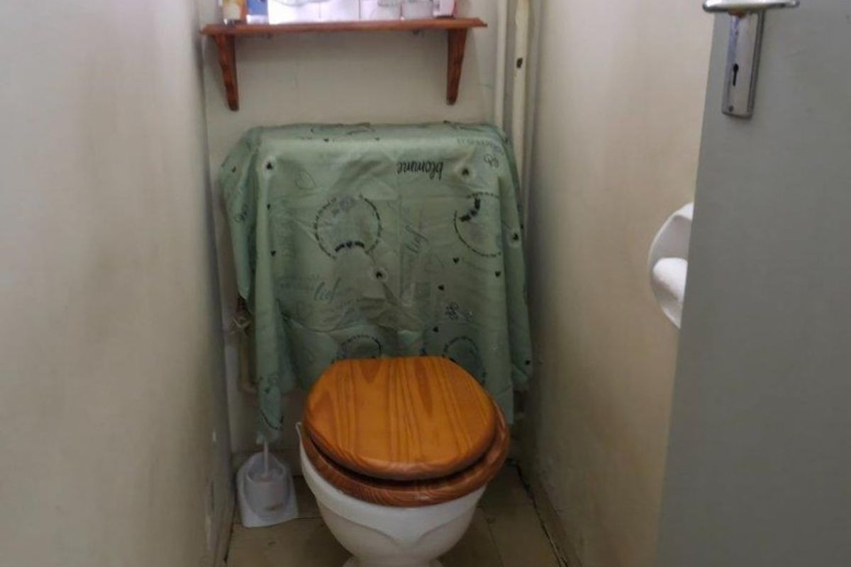 A compact bathroom featuring a standard toilet, tiled flooring, and a wall-mounted storage shelf.