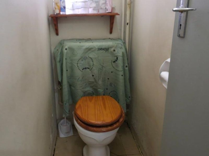 A compact bathroom featuring a standard toilet, tiled flooring, and a wall-mounted storage shelf.