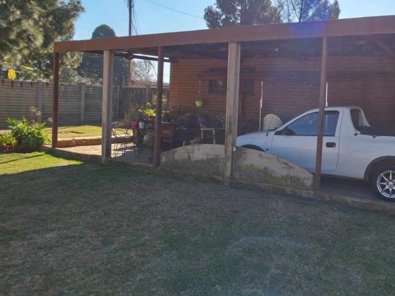 A covered outdoor patio area featuring brick construction and concrete paving, providing a functional space for outdoor living and vehicle shelter.
