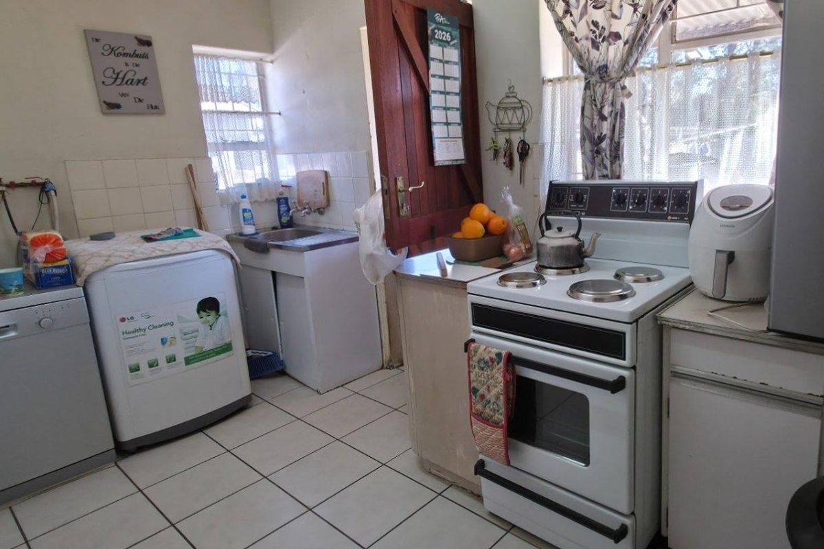 A functional kitchen area featuring tiled flooring, a stainless steel sink, and a freestanding stove with built-in cabinetry and tiled splashbacks.
