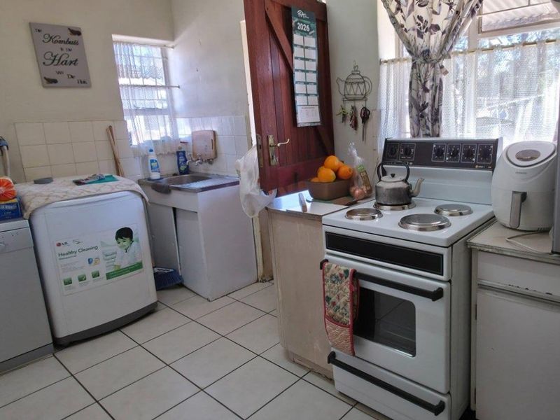 A functional kitchen area featuring tiled flooring, a stainless steel sink, and a freestanding stove with built-in cabinetry and tiled splashbacks.