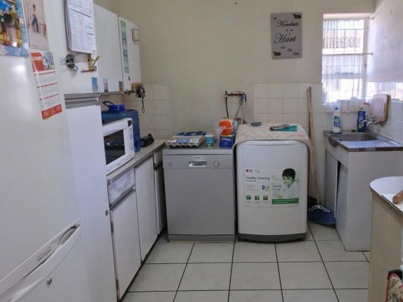 Functional laundry area featuring tiled flooring, a stainless steel sink, and built-in cabinetry with space for appliances.