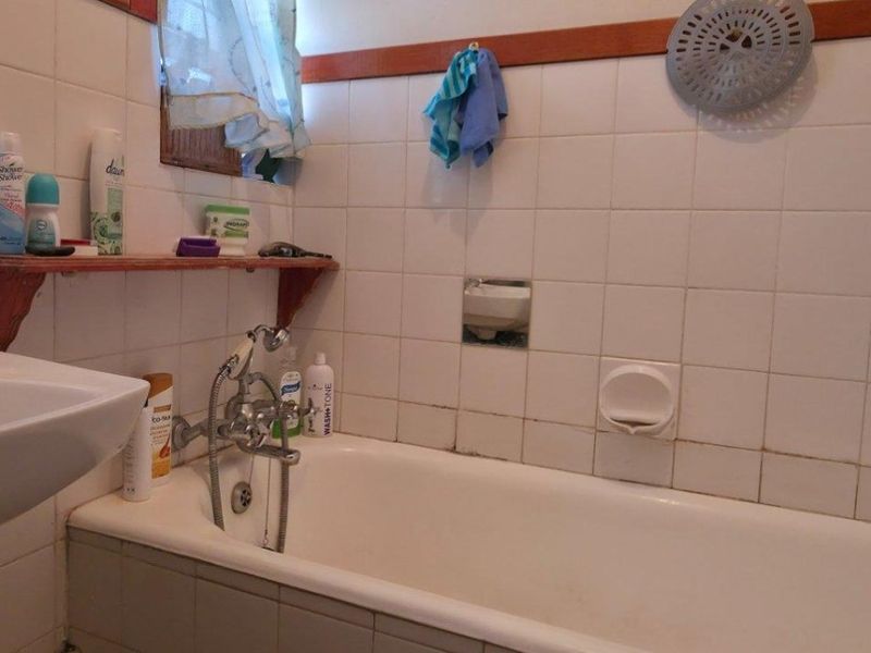 A functional bathroom featuring a bathtub with a handheld shower attachment and tiled walls, showing signs of age and wear.