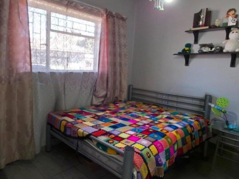 A standard bedroom featuring tiled flooring and a window fitted with security bars.