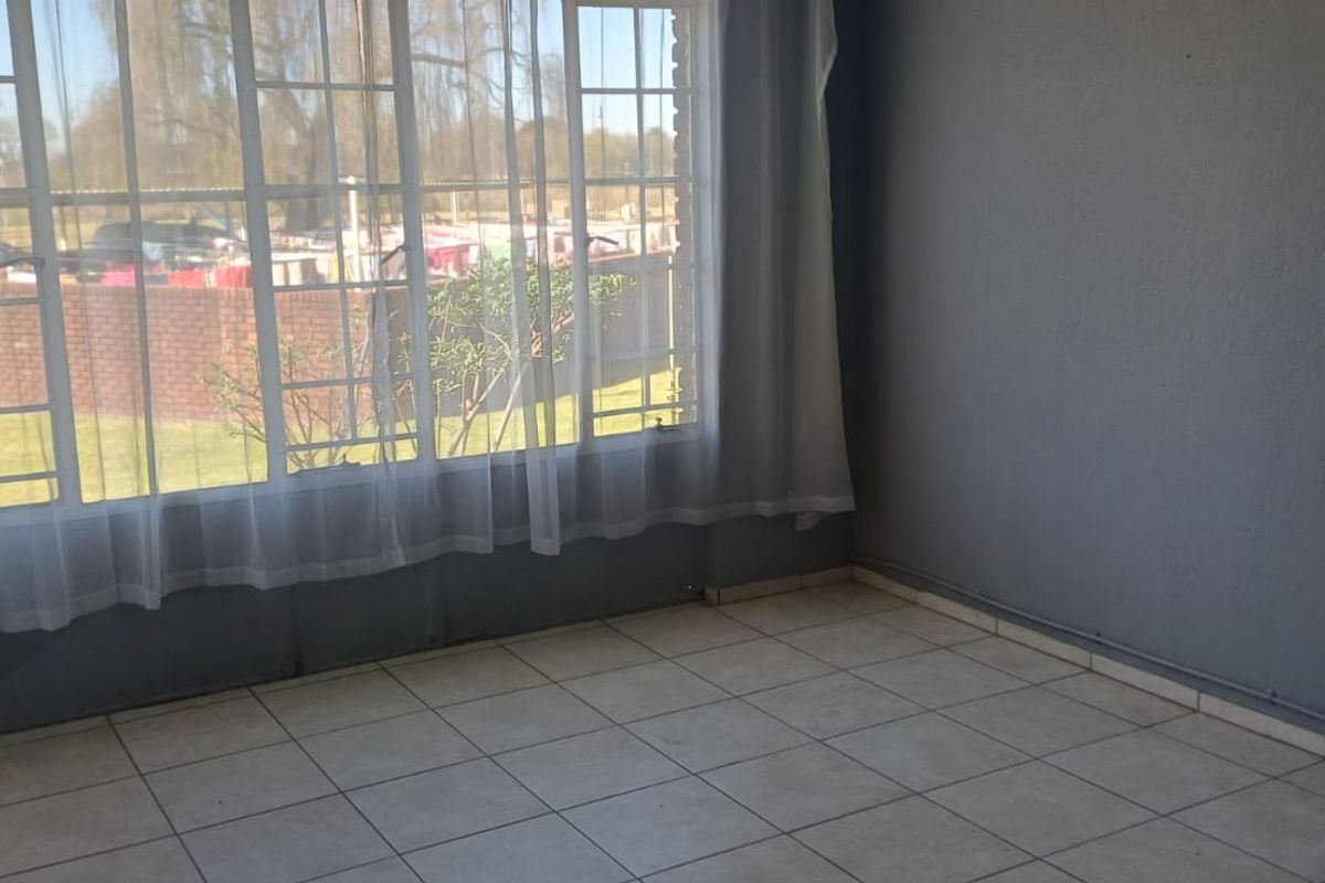 An empty living room featuring tiled flooring and a large window with security bars, offering a view of the exterior garden area.