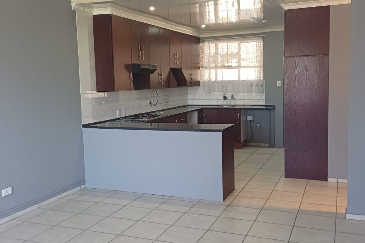 A functional kitchen featuring dark wood cabinetry, granite countertops, a gas hob with extractor fan, and tiled flooring in an open-plan layout.