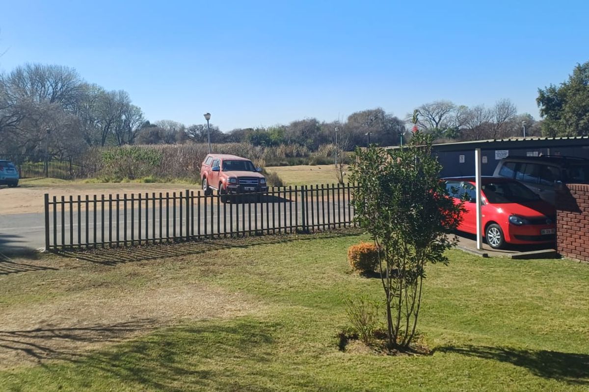 A view of the rear garden area featuring a lawn, brick boundary wall, and a covered carport structure.