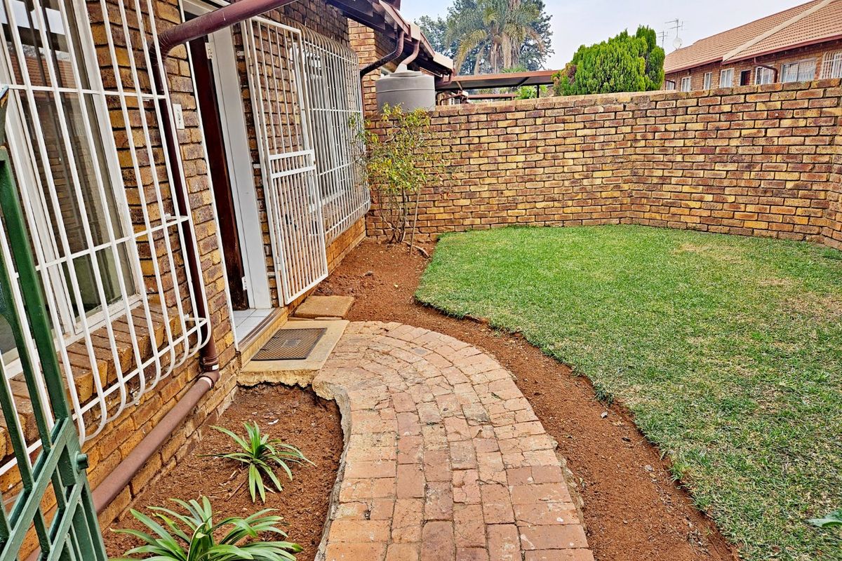 A private rear garden featuring a brick-paved pathway, a well-maintained lawn, and secure access points with fitted security gates and bars.