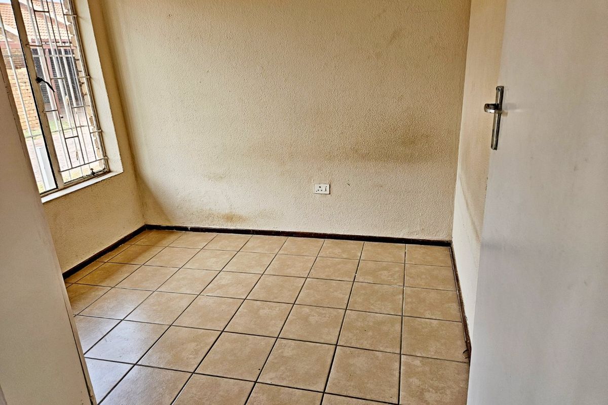 An empty bedroom featuring tiled flooring and security bars on the window, requiring cosmetic updates to the wall finishes.