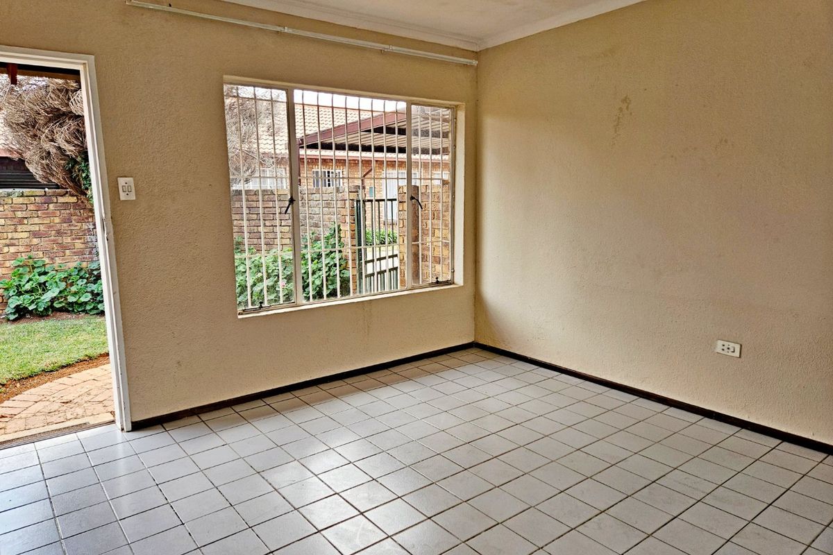 An empty living room featuring tiled flooring, security bars on the windows, and direct access to the outdoor area.