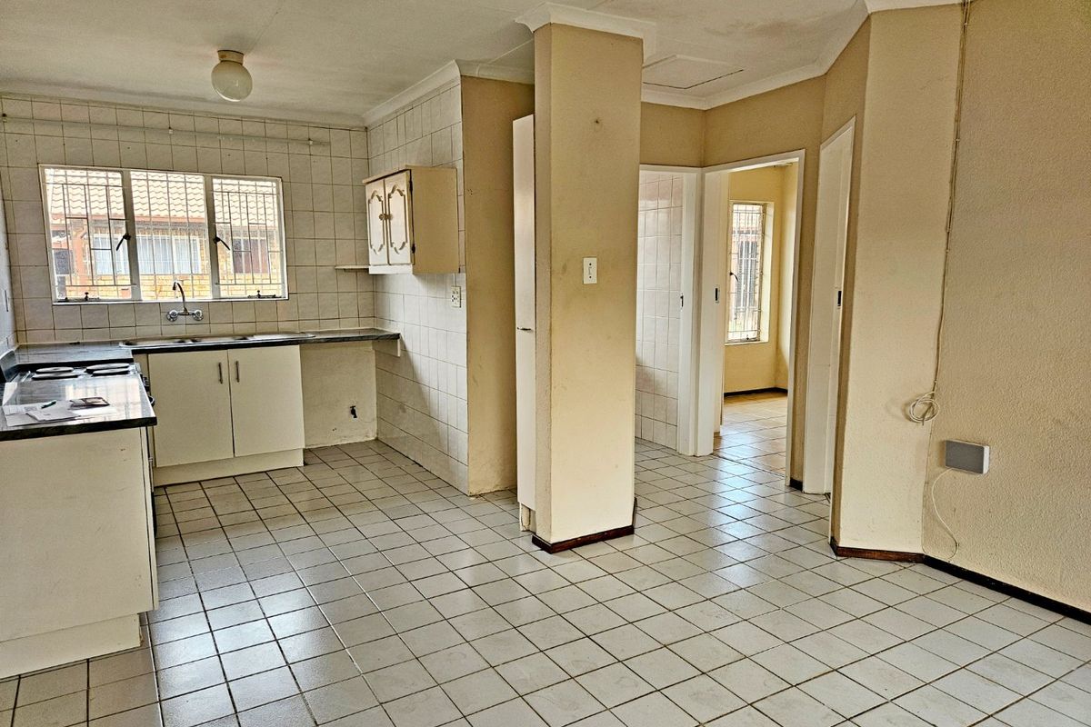 An empty, dated kitchen featuring tiled flooring, tiled splashbacks, and built-in cabinetry, offering a blank canvas for renovation.