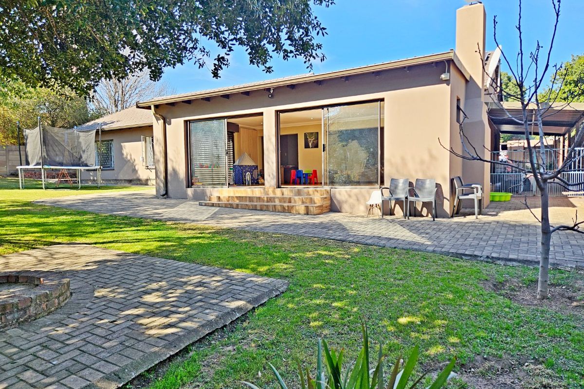 Rear view of the house featuring a paved patio area, large sliding glass doors, and an external chimney stack.