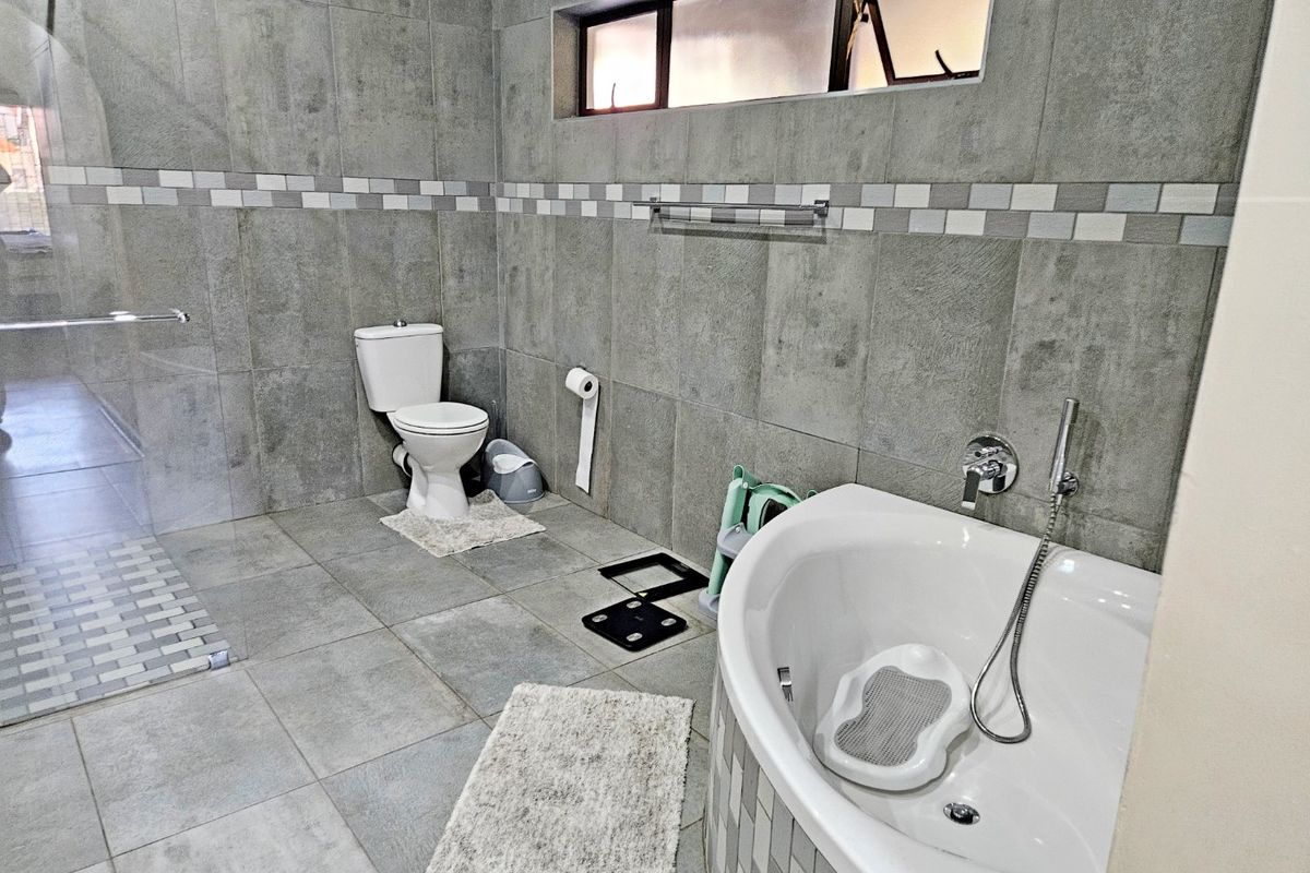 Modern bathroom featuring grey tiled walls and flooring, a walk-in shower, and a contemporary bathtub with chrome fixtures.