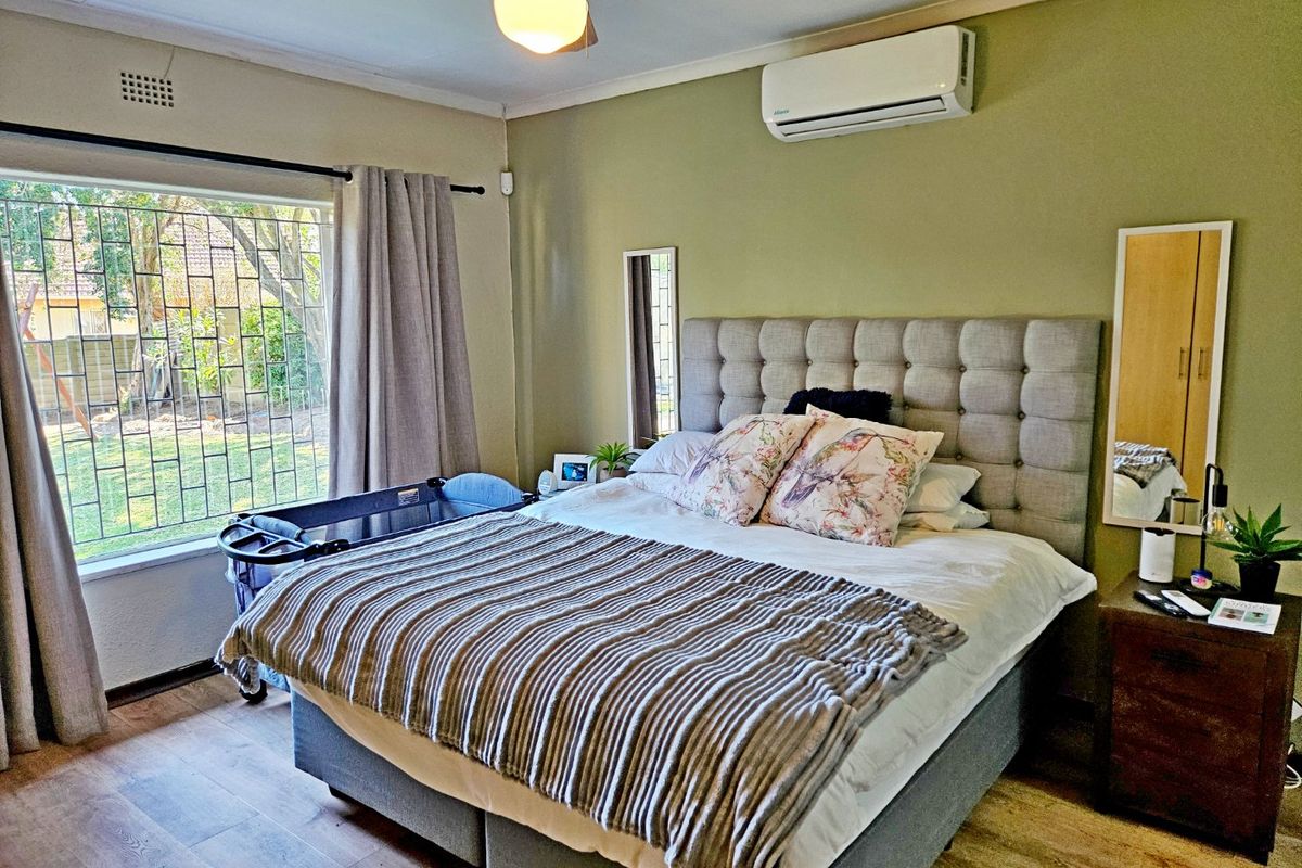 A well-maintained bedroom featuring laminate flooring, a ceiling fan, and a wall-mounted split-system air conditioner with security bars on the window.