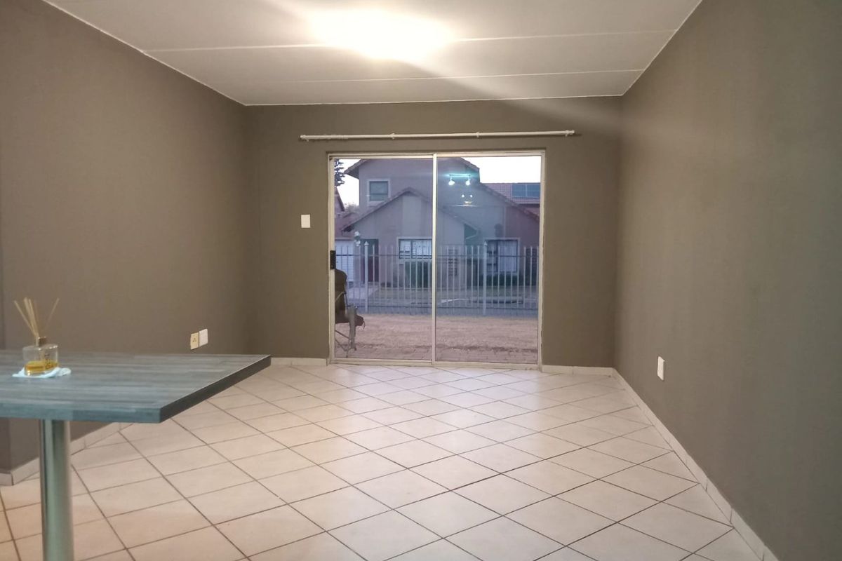 An open-plan living area featuring neutral wall tones, tiled flooring, and a sliding glass door providing access to the exterior.