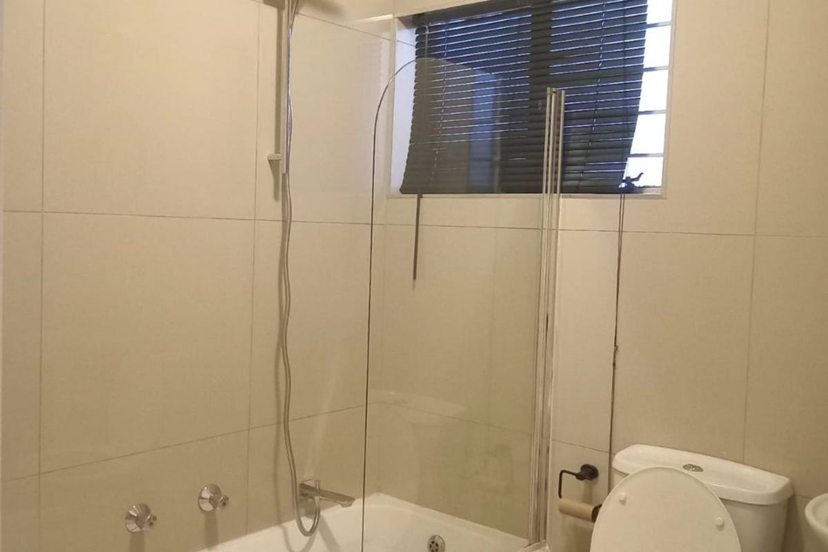 A clean, modern bathroom featuring a bathtub with a glass shower screen, a toilet, and neutral wall tiling.