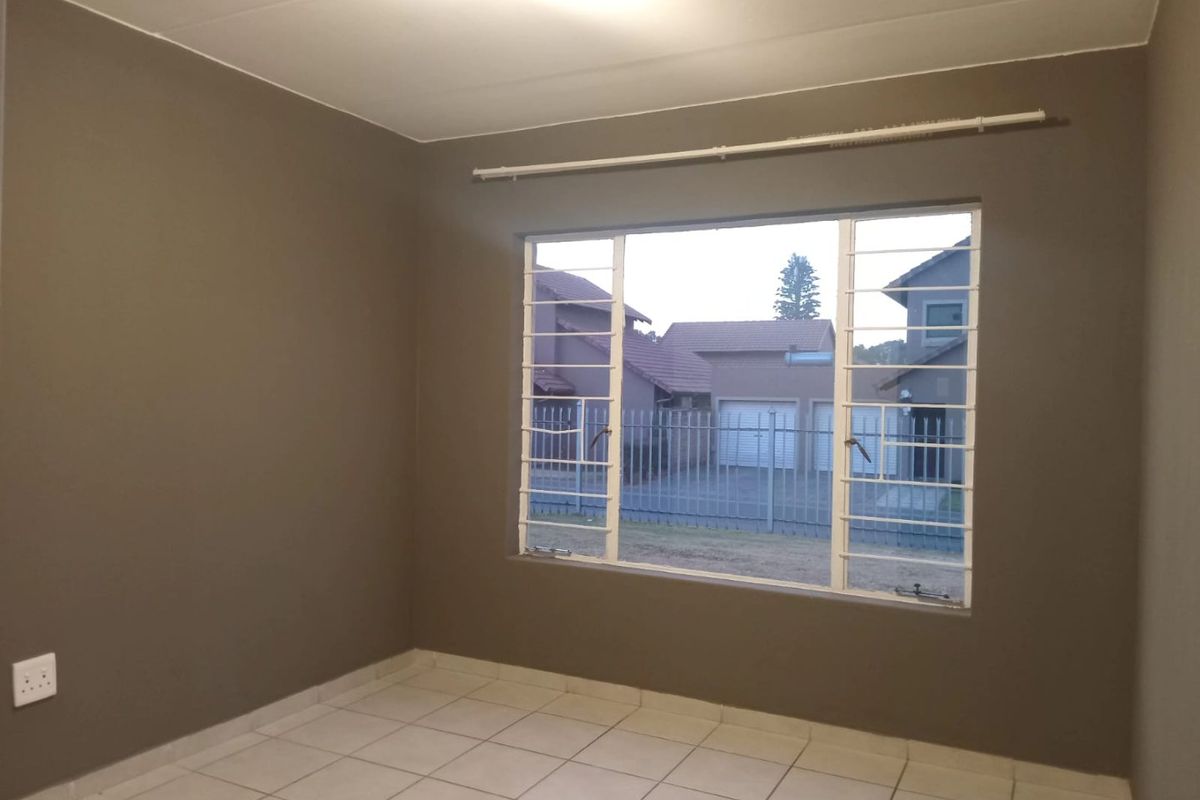 An empty bedroom featuring neutral-toned walls, tiled flooring, and a large window fitted with security bars.
