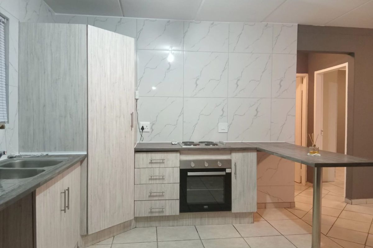 A functional kitchen featuring light wood-grain cabinetry, marble-look tiled backsplash, built-in oven and hob, and a convenient breakfast bar extension.