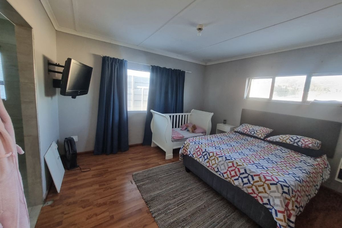 A functional bedroom featuring laminate flooring, wall-mounted television bracket, and natural light through multiple windows.