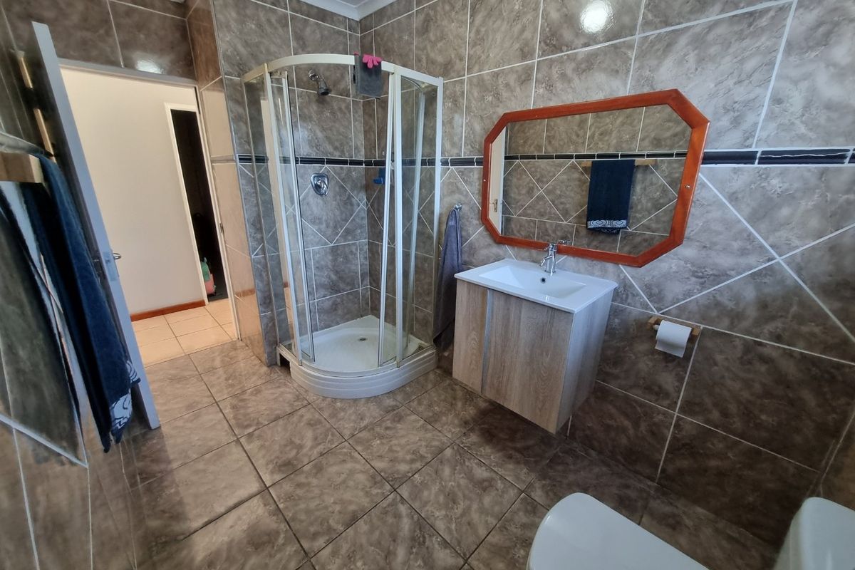 A functional bathroom featuring a corner shower enclosure, wall-mounted vanity with basin, and full-height wall tiling.