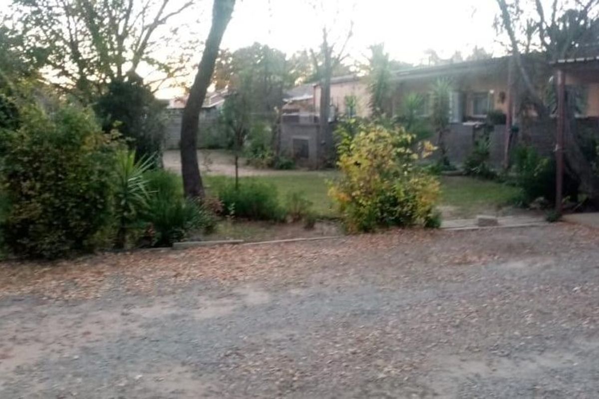 Rear exterior view of the property featuring a gravel driveway, carport, and established garden area with boundary walling.