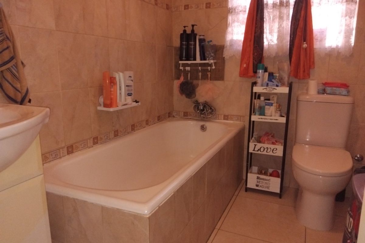 A functional bathroom featuring a built-in bathtub, pedestal basin, and toilet with neutral ceramic wall and floor tiling.