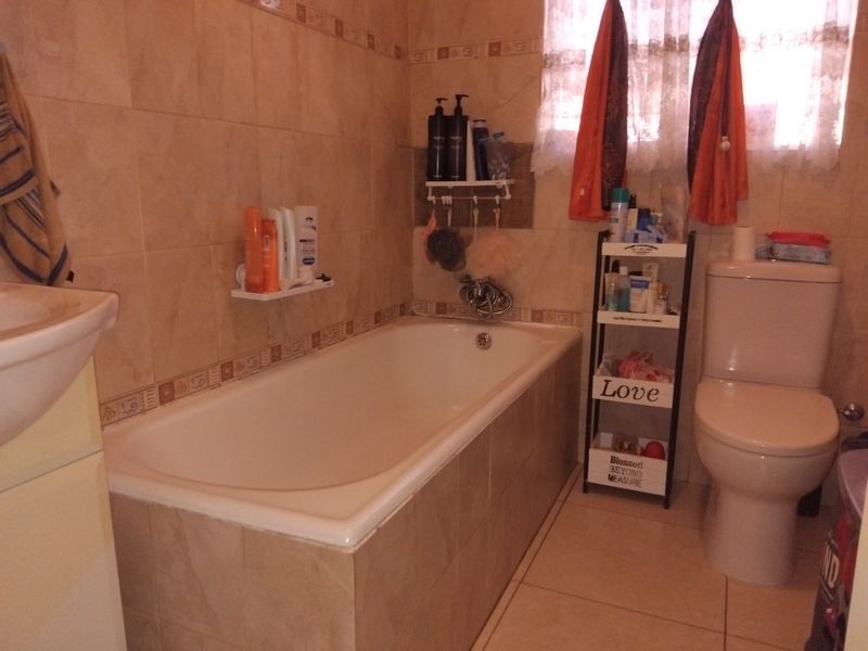 A functional bathroom featuring a built-in bathtub, pedestal basin, and toilet with neutral ceramic wall and floor tiling.